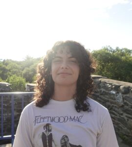 Olivia wears a Fleetwood Mac shirt with sub and brink wall behind her.