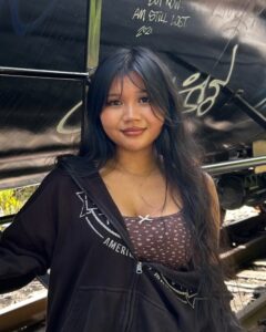 Mea Ree with hair down and sweatshirt on one shoulder in front of graffiti on a train