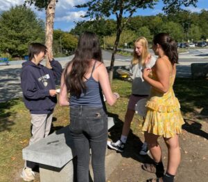 Group of five high school students stand in a circle around a stone bench